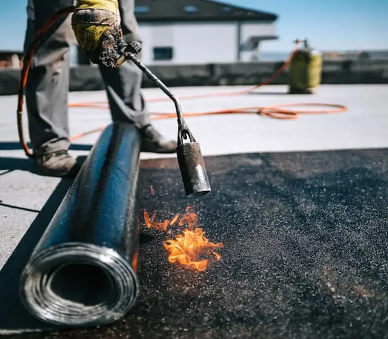 Roofer torching down a membrane on a flat commercial roof